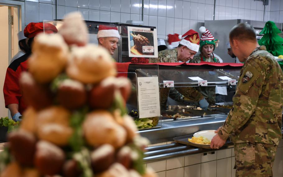 Commander of the 9th Air and Space Expeditionary Task Force - Afghanistan, Maj. Gen. James B. Hecker, center, in the Santa hat with antlers, and Chief Master Sgt. Lisa Arnold, the unit's command cheif master sergeant, right, in the elf hat, serve Christmas Day dinner at a dining facility on Resolute Support headquarters in Kabul, Afghanistan on Monday, Dec. 25, 2017.
