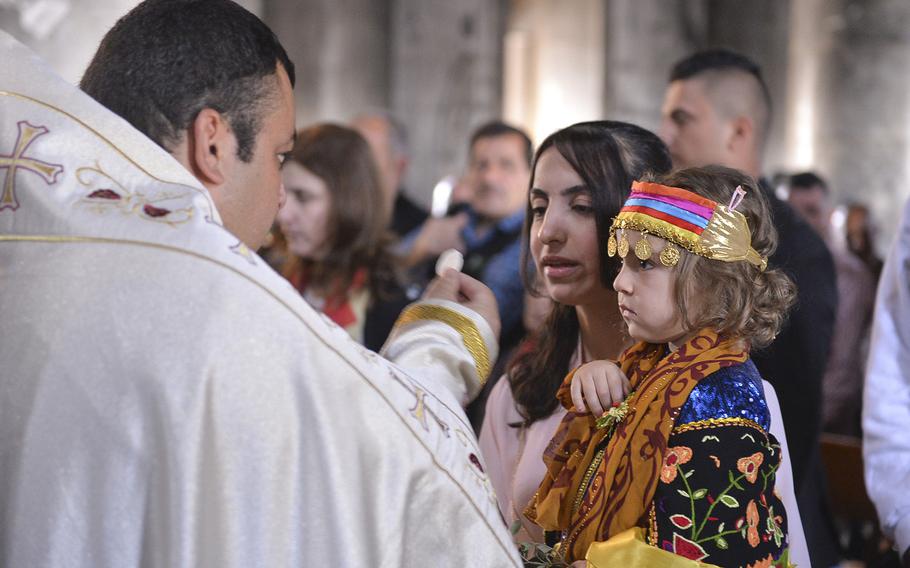 A woman receives the eucharist during Palm Sunday Mass at the Church of the Immaculate Conception in Qaraqosh on March 9, 2017, while a child in a traditional outfit looks on. Former residents of the town, forced to fee when Islamic State militants advanced in August 2014, returned briefly to mark the holy day, but few have returned permanently since it was freed from ISIS in October 2016.





