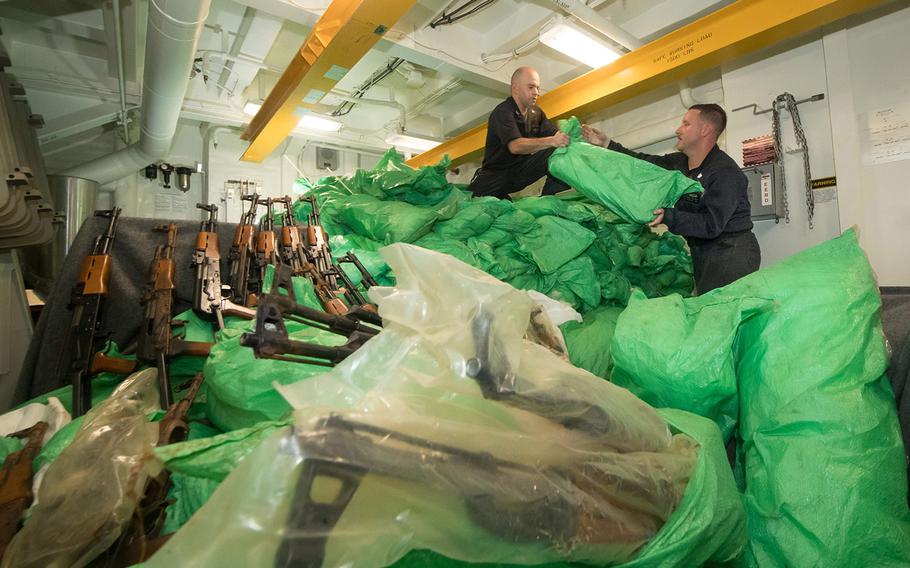 Petty Officer 1st Class Griffin Vancil, left, and Petty Officer 1st Class Devan Wallswolf stack a cache of over 1,000 AK-47 automatic rifles aboard the guided-missile destroyer USS Jason Dunham on Aug. 30, 2018. The ship’s visit, board, search and seizure team seized the weapons from a skiff during a flag verification boarding near Yemen as part of maritime security operations. 