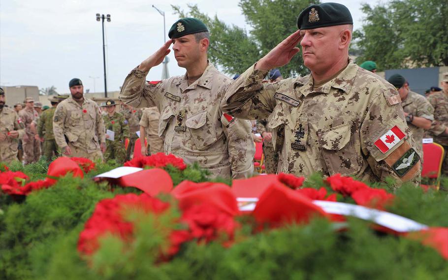Canadian Armed Forces Major-General Dany Fortin, left, commander of the 1st Canadian Division Headquarters, and Sen. Appointment Chief Warrant Officer Merry salute and show their respect to a centerpiece covered in memorial reefs at the Armistice Ceremony at Union III, Baghdad on Nov. 11, 2018.