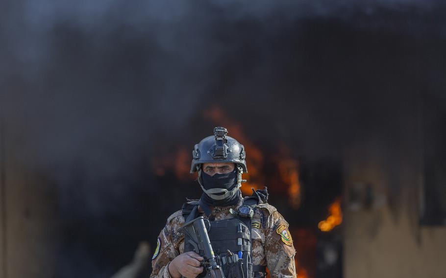 An Iraqi soldier stands guard in front of smoke rising from a fire set by pro-Iranian militiamen and their supporters in the U.S. embassy compound, Baghdad, Iraq, Wednesday, Jan. 1, 2020.