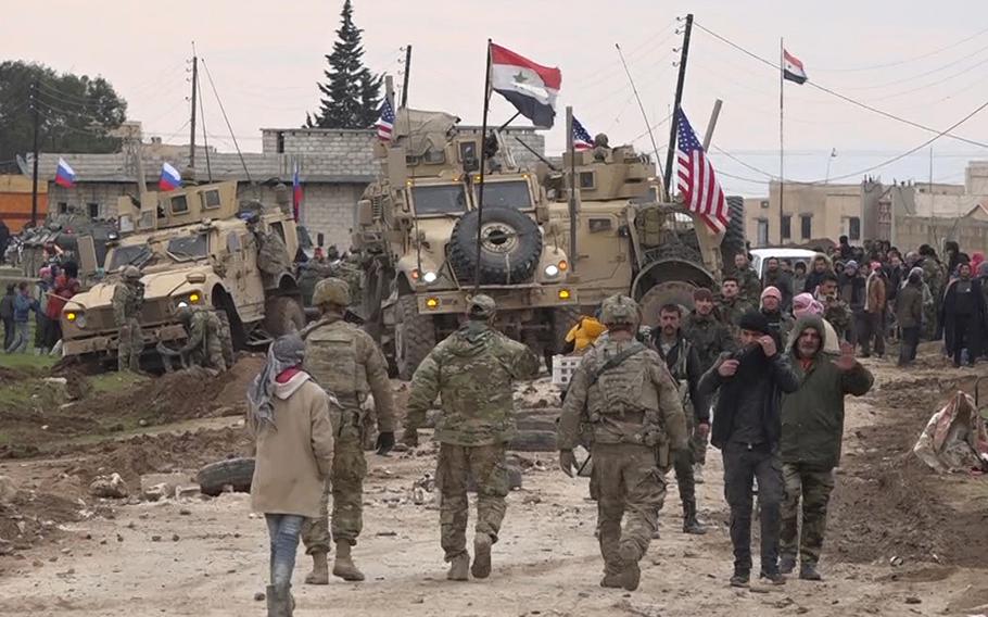 In this frame grab from video, Russian, Syrian and others gather next to an American military convoy stuck in the village of Khirbet Ammu, east of Qamishli city, Syria, Wednesday, Feb. 12, 2020. Syrian media and activists say a Syrian was killed and another wounded in a rare clash between American troops and a group of government supporters in northeast Syria. 