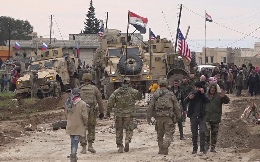 In this frame grab from video, Russian, Syrian and others gather next to an American military convoy stuck in the village of Khirbet Ammu, east of Qamishli city, Syria, Wednesday, Feb. 12, 2020. Syrian media and activists say a Syrian was killed and another wounded in a rare clash between American troops and a group of government supporters in northeast Syria.