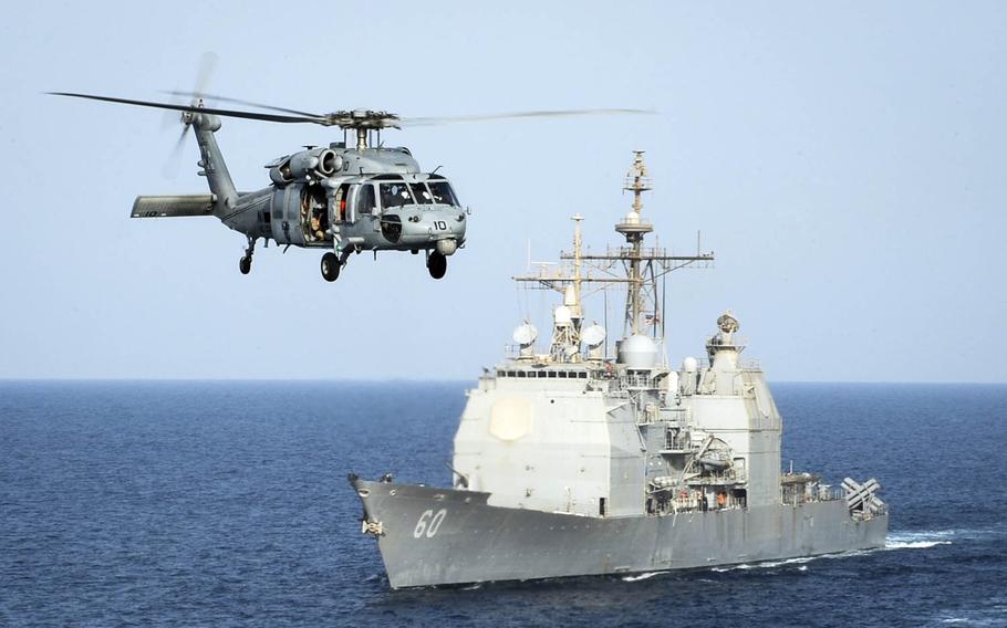 An HH-60H Sea Hawk helicopter passes the guided-missile cruiser USS Normandy in the Arabian Gulf in September 2015.