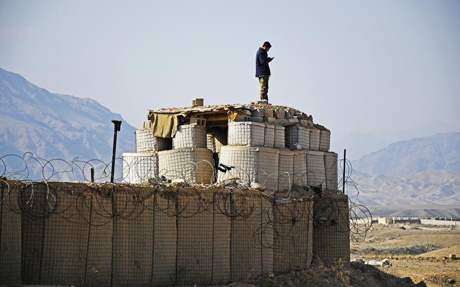 An Afghan soldier checks his cellphone on Saturday, Feb. 22, 2020, atop the walls of his base, just east of Kabul, during the first day of an agreed reduction of violence between the Taliban and the U.S. forces. Government forces are also to stand down, said Gawhar Khan Baburi, the district governor of Surobi.
