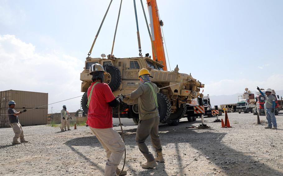 Civilian contractors prepare to load a Mine Resistant Ambush Protected vehicle on to a flatbed trailer during the Army Field Support Battalion - Afghanistan, 10th Mountain Division Resolute Support Sustainment Brigade retrograde cargo operation on Bagram Air Field, Afghanistan July 12, 2020. Many troops who deployed to the country this year spent their time there helping with the U.S. drawdown.