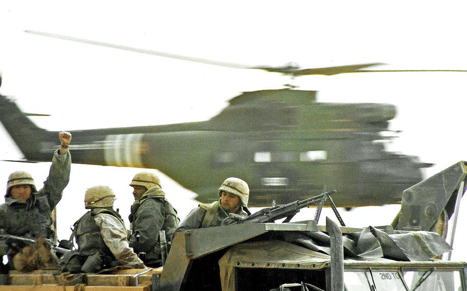 An allied helicopter flies past U.S. troops moving to the Iraqi border to begin the Operation Desert Storm ground assault in February 1991. 

