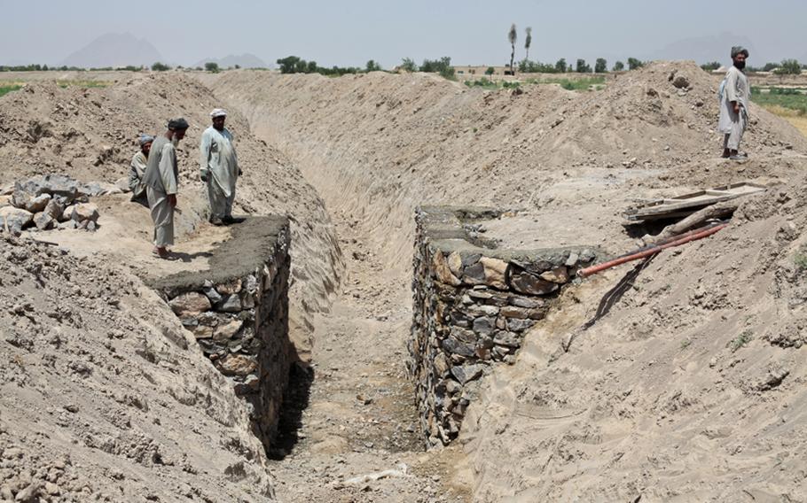 Villagers stand beside a new bridge and irrigation canal being dug using U.S. and Canadian development money near the village of Zormashor, in Dand district, Kandahar province, Afghanistan. June 27, 2010. U.S. troops in the district can&#39;t patrol in the village 24 hours a day, so they rely on an armed "village security team" to guard the project against Taliban attack. June 27, 2010.