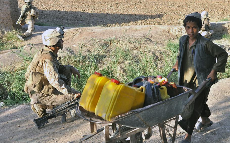 An Afghan boy pushes a wheelbarrow home from the field past a Marine from A Company, 1st Battalion, 6th Marines in Marjah District on June 19. Firefights and IEDs in the area are frequent.