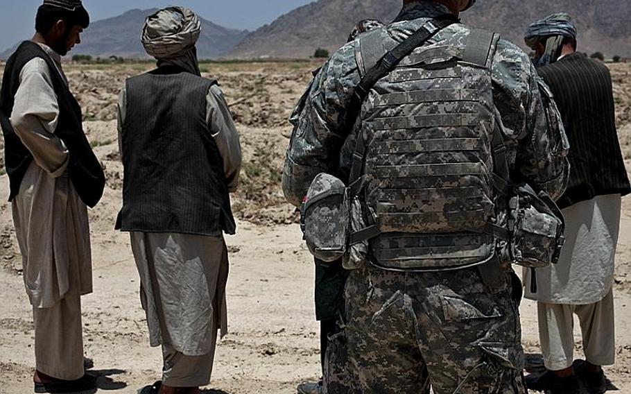Pfc. Jesse Zurcher, of 1st Squadron, 71st Cavalry Regiment, stands guard over a group of Afghan men at a traffic checkpoint in Dand district, Kandahar province, Afghanistan. June 18, 2010.