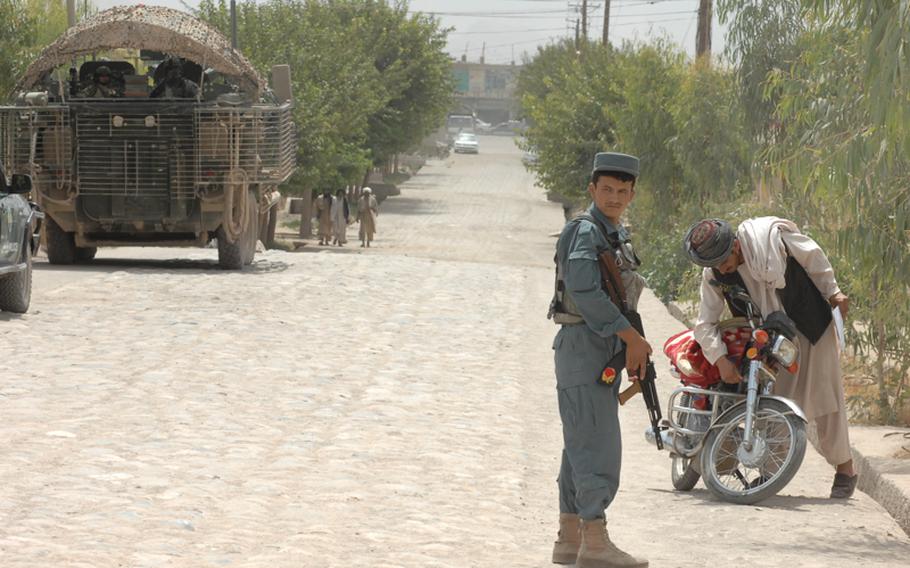 An Afghan police officer is poised to talk to a motorcyclist recently while members of 1st Squadron, 2nd Stryker Cavalry Regiment wait nearby in Tirin Kot.