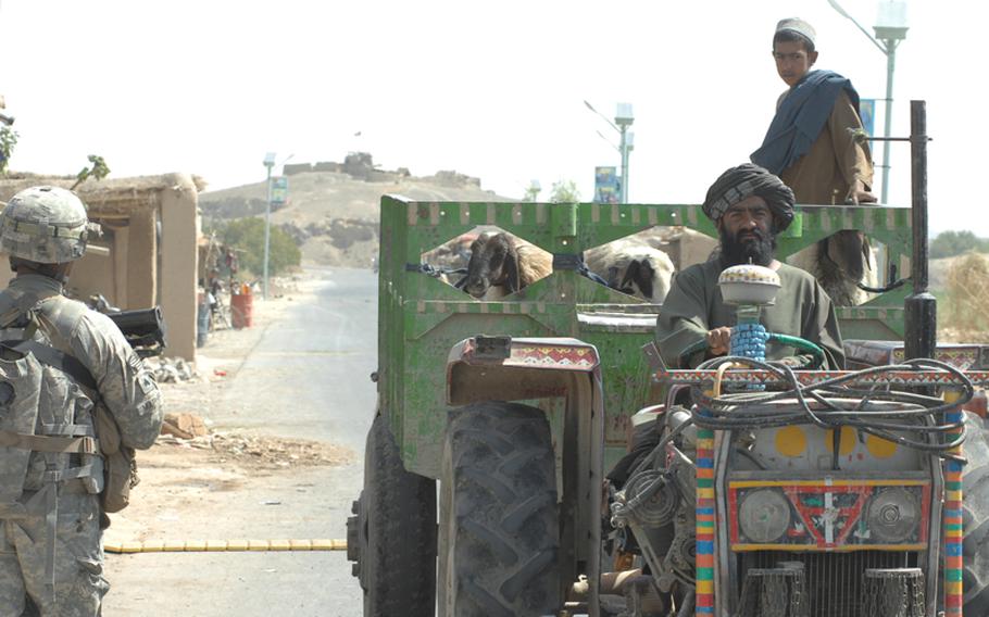 A farmer passes Sgt. Baholo Maphiri, 33, of the 2nd Stryker Cavalry Regiment. An Afghan National Police outpost watches the road at a distance.