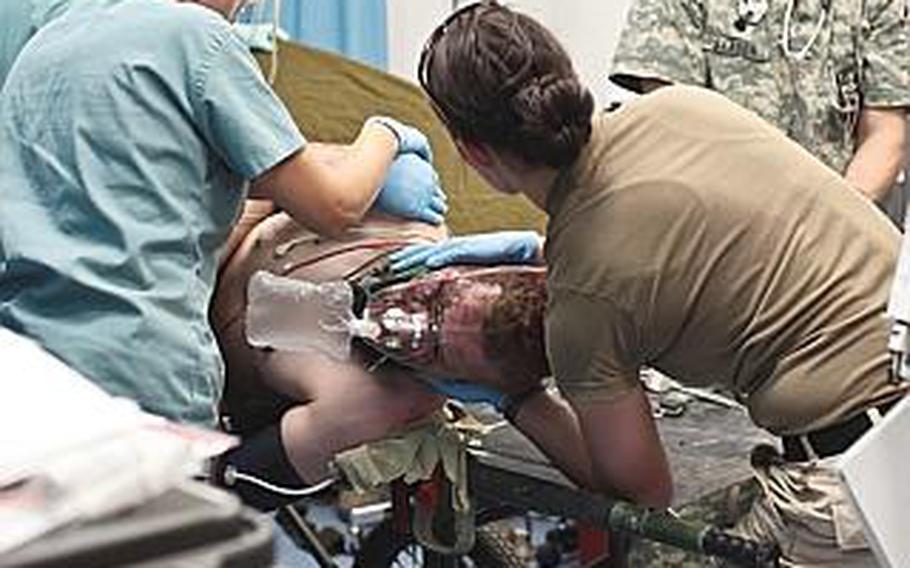 Trauma room staff at Kandahar Airfield's Role 3 hospital roll a wounded U.S. soldier over onto his side to check for injuries to his back. Although the soldier had been wounded in a bomb blast and received extensive shrapnel wounds to his face and side, none of his injuries were life-threatening. 