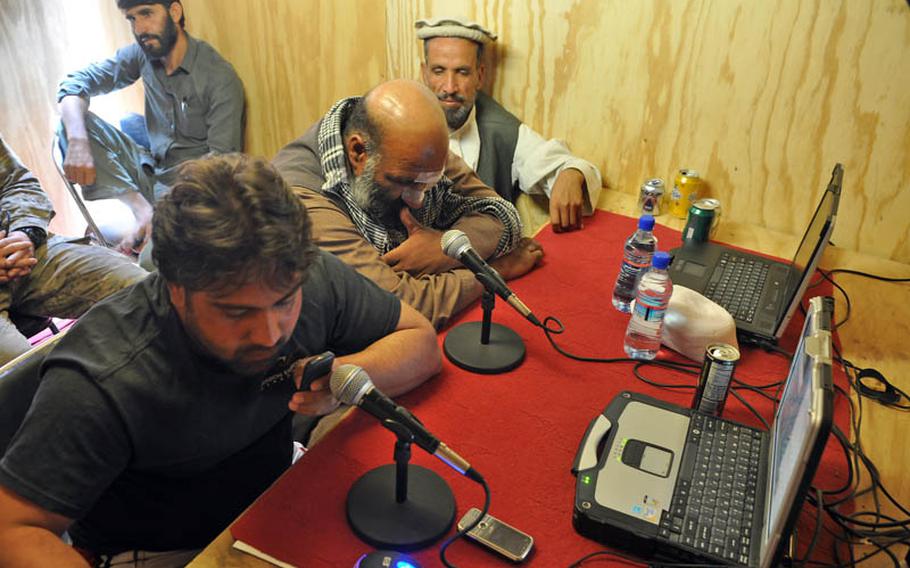 Shamla Voice host Gulab Kochai takes a call Friday inside the broadcast booth on COP Nerkh. Beside him, local police commander Mohammad Gul Torkai and Afghan National Police Colonel Mohammed Faroq Sidiqi (wearing cap) listen in.