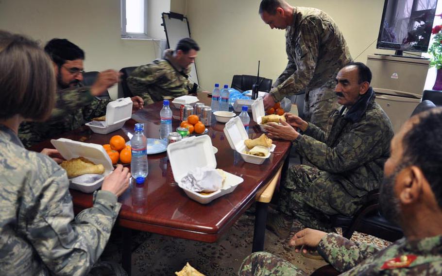 Air Force Lt. Col. Michael Needham, standing, and his Afghan counterpart, Col. Mahmood Ur Rahman, middle right, sit down to a lunch of Afghan cuisine during a lunch break at Pohantoon-e-Hawayee (the Afghan Air Force College). At the college, as well as at the Thunder Lab program for prospective pilots, Coalition mentors, like Needham, have made a point of sitting down to meals to build camaraderie with their Afghan Air Force counterparts.