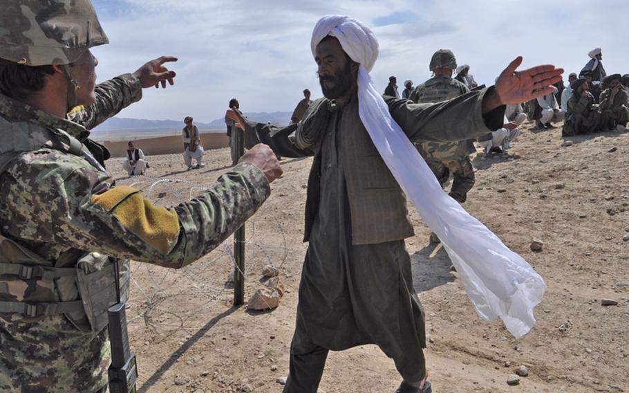 An Afghan soldier searches villagers at the entrance to a shura in Ghorak district, Kandahar province.