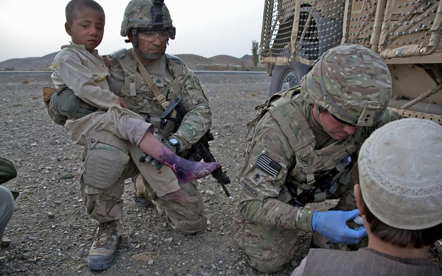 Sgt. Ramon Cortez, 38, a forward observer from El Paso, Texas, holds a young Afghan boy whose foot was badly burned. Injuries such as burns and broken fingers are often treated by Afghan doctors with little more than colored dye in this part of Khost province, despite the fact there is a government hospital less than 10 miles away down the paved road seen in the background.