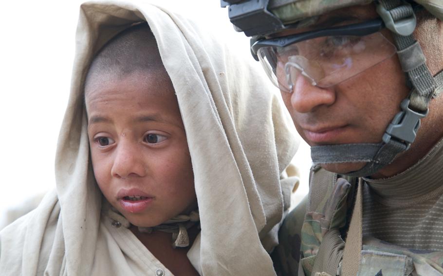 Sgt. Ramon Cortez, 38, a forward observer from El Paso, Texas, holds a young boy with two burned feet as a medic treats the wounds. Despite the severity of the burns, the boy barely flinched while the medic worked on him.
