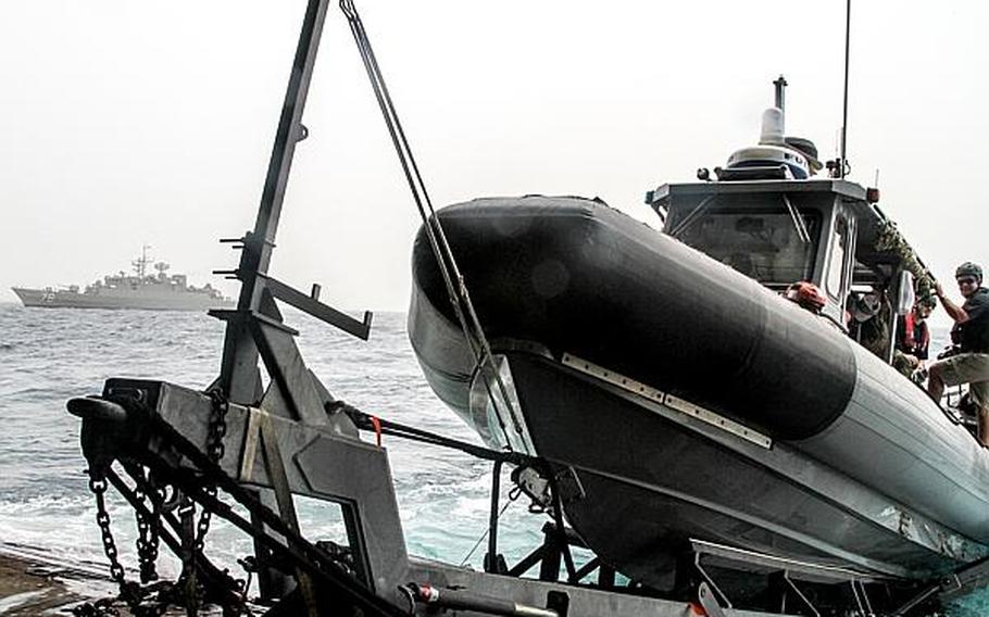 An Iranian navy ship sailed by in the background while sailors aboard the USS Ponce were preparing to launch a rigid-hulled inflatable boat as part of an international mine countermeasure exercise in the Persian Gulf.