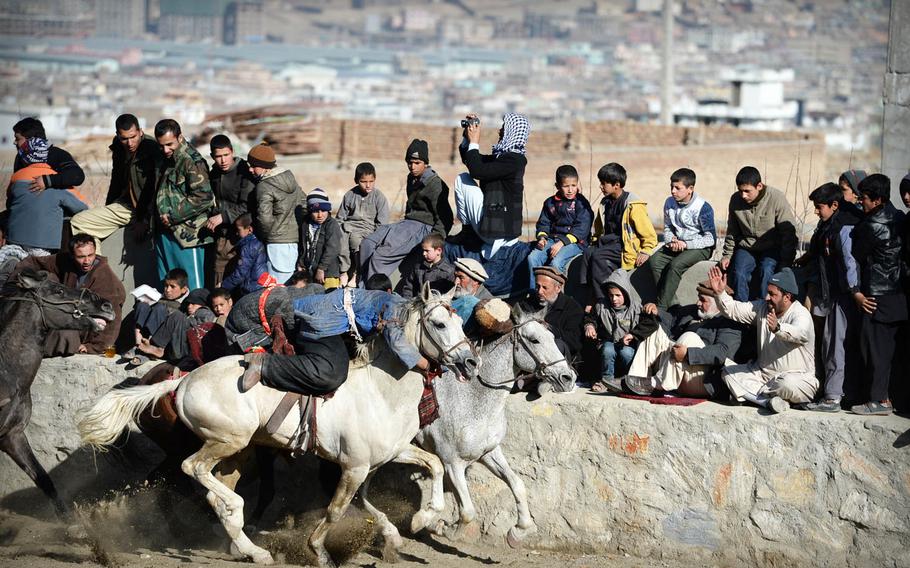 Spectators lift their legs to get out of the way of buzkashi riders during a match on Thursday, Jan. 15, 2015 in Kabul. Men and boys trickled in to watch as the game stretched on for hours.
