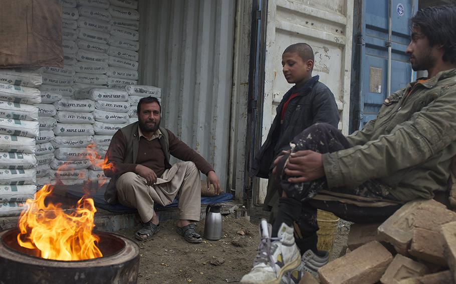 Construction supply store owner Shafiq warms up in front of his shop with his family Jan. 21, 2015. His business has been on Jalalabad Road for eight years, and he says that 2014 was the most violent he's seen.