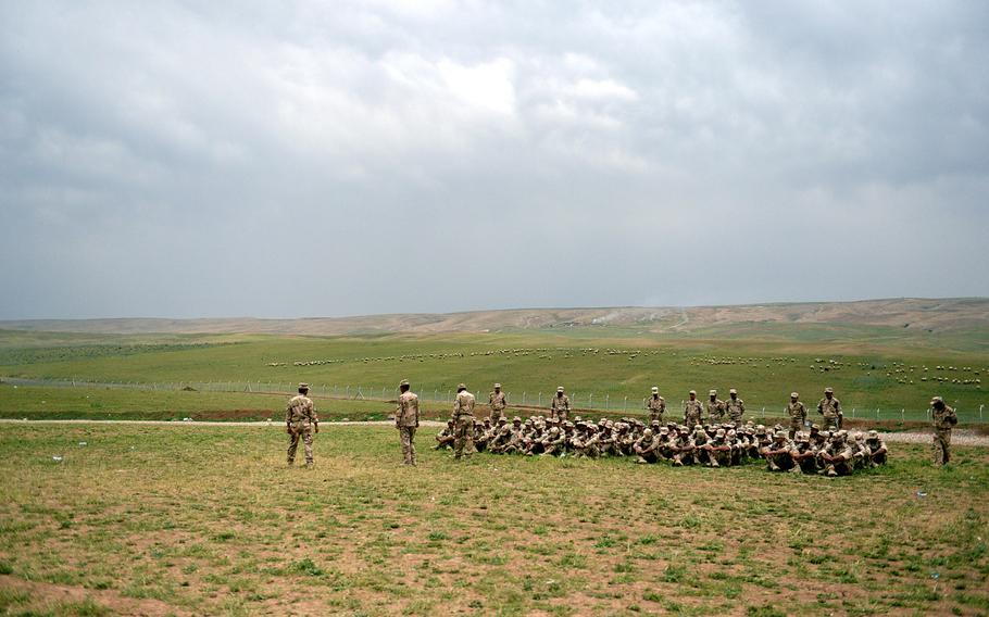 As sheep graze in the background, volunteer fighters listen to an instructor at a camp in northern Iraq. The volunteers, who are training to fight the Islamic State group, have only a few broken weapons to train with.