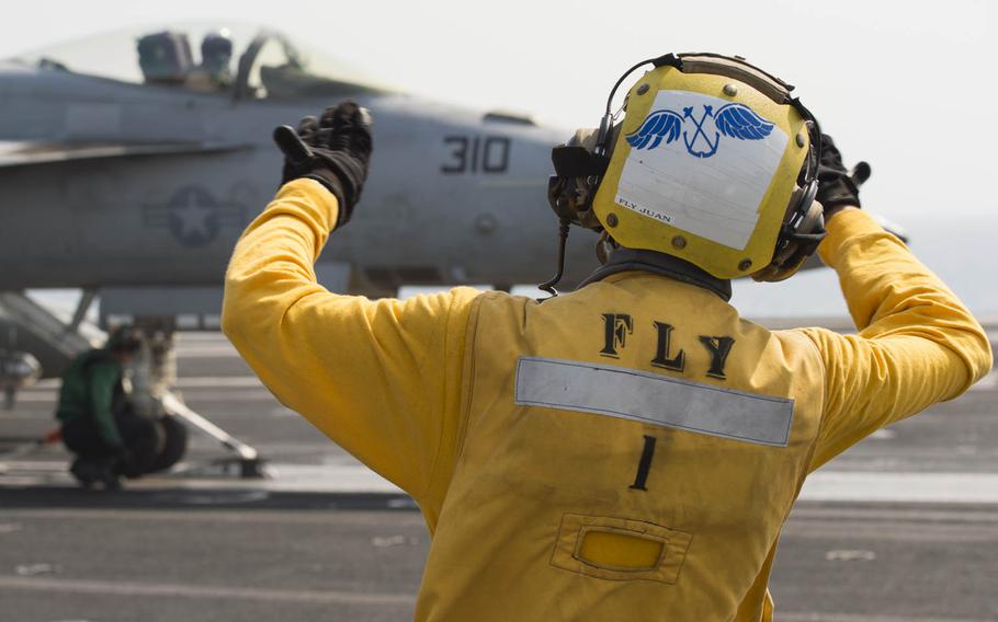 A member of the flight deck crew aboard the aircraft carrier USS Theodore Roosevelt directs the pilot of an F/A-18 Super Hornet prior to launch Aug. 13, 2015.  Flight deck crew use hand signals to communicate with the pilots to ensure proper protocol is followed and to reduce risk of an accident.
