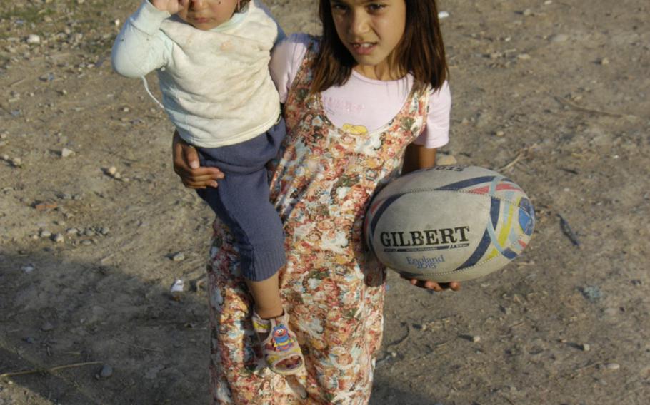 This young Yazidi girl has her hands full, with a rugby ball in one hand, and a toddler in the other at a camp for displaced people in Irbil, Iraq, on Oct. 25, 2015.