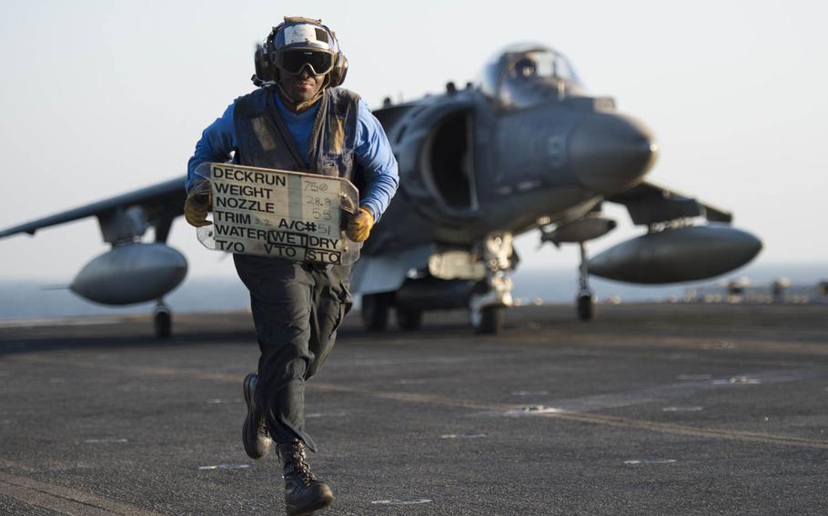 Navy Airman David Dorsaima, a tote board operator, gets out of the way  after showing the Marine pilot of an AV-8B Harrier from the 15th Marine Expeditionary Unit the specifications the aircraft is required to conform to prior to launching off the flight deck of the USS Essex, Oct. 13, 2015.