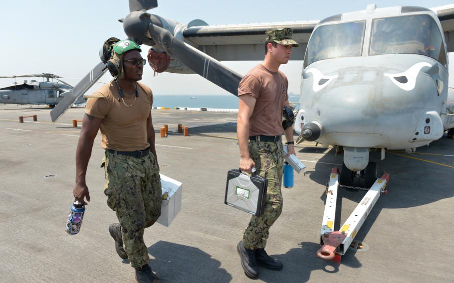 Sailors transit the flight deck in front of a MV-22 Osprey tilt-rotor aircraft on board the amphibious assault ship USS Boxer on Aug. 1, 2019. 