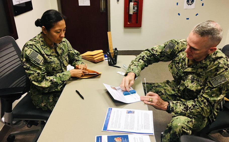Navy Capt. Charles McDermott, right, provides a cheek swab as Lt. Marisol Armora explains the procedure during a bone marrow drive at Naval Amphibious Task Force 51/5 headquarters in Bahrain on Oct. 24, 2019.