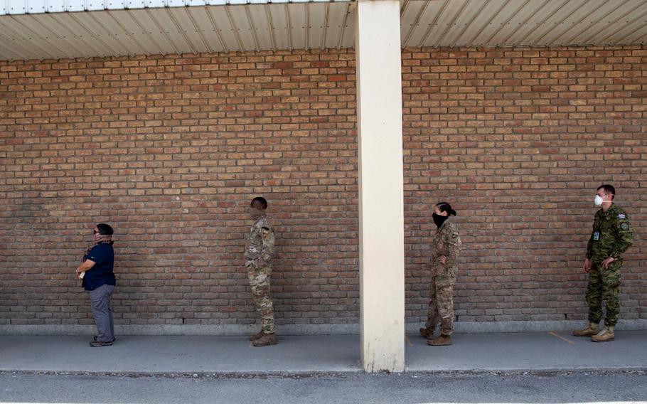 NATO Resolute Support service members and civilians wait for lunch at a dining facility in Kabul, Afghanistan, April 10, 2020. Personnel at RS must wear face coverings and stay six feet apart while waiting in line to receive a to-go meal as part of COVID-19 prevention measures.