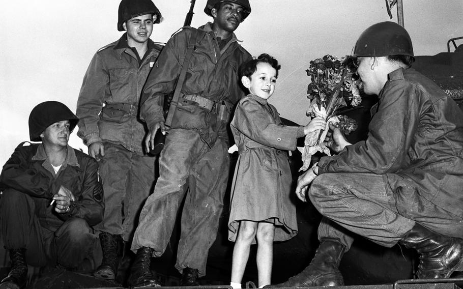 Seven-year-old Jacques Loisy presents a bouquet to Sgt. Kenneth Gammons during ceremonies commemorating the tenth anniversary of the liberation of Nancy by Allied troops during World War II. Looking on are, left to right, Sgt. Samuel Henricks, Pvt. Joseph Hafele and Pfc. Alfred Allen.