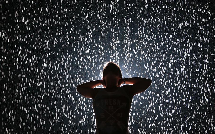 Jin Lee, a student designer from New York, experiences Random International's "Rain Room" at the Museum of Modern Art (MoMA) on Friday, July 19, 2013, in New York. Visitors wait as much as four hours to interact with the field of rain-like water, which pauses wherever a human body is detected, allowing visitors "the experience of controlling the rain."  (AP Photo/Bebeto Matthews, File)