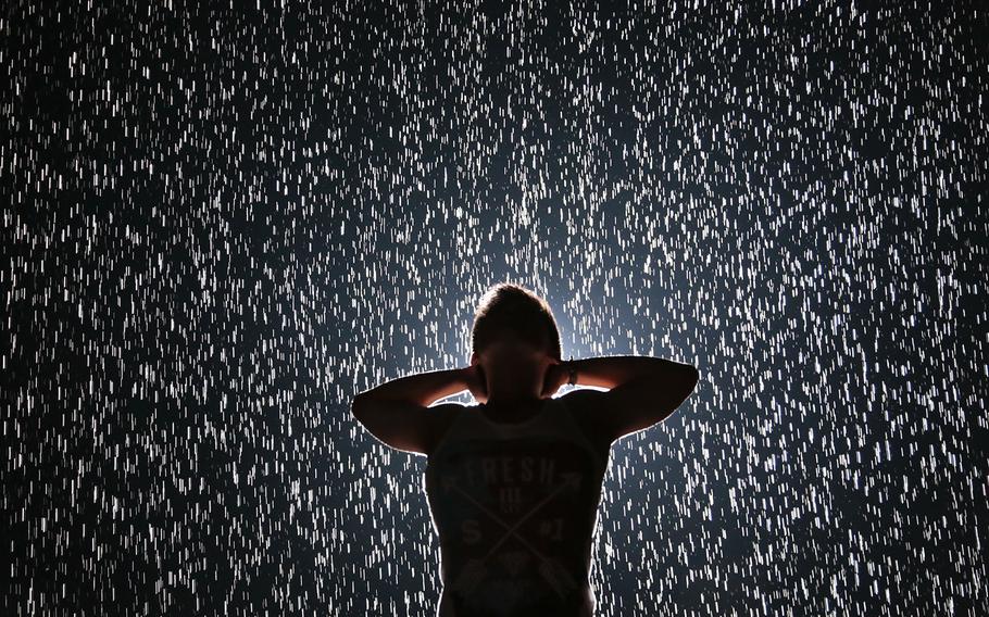 Jin Lee, a student designer from New York, experiences Random International's "Rain Room" at the Museum of Modern Art (MoMA) on Friday, July 19, 2013, in New York. Visitors wait as much as four hours to interact with the field of rain-like water, which pauses wherever a human body is detected, allowing visitors "the experience of controlling the rain."  (AP Photo/Bebeto Matthews, File)