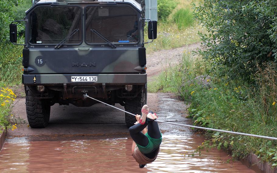 A competitor traverses a rope hanging over a muddy pool in the Shock 'N Rock: Reloaded obstacle course event.