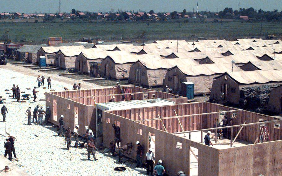 Members of Naval Mobile Construction Battalion 133 and Brown & Root workers construct SEA huts at Camp McGovern in May, 1998. The huts, which are to replace the tents in the background, feature linoleum floors and heating/air conditioning units. In the distance is part of the city of Brcko.