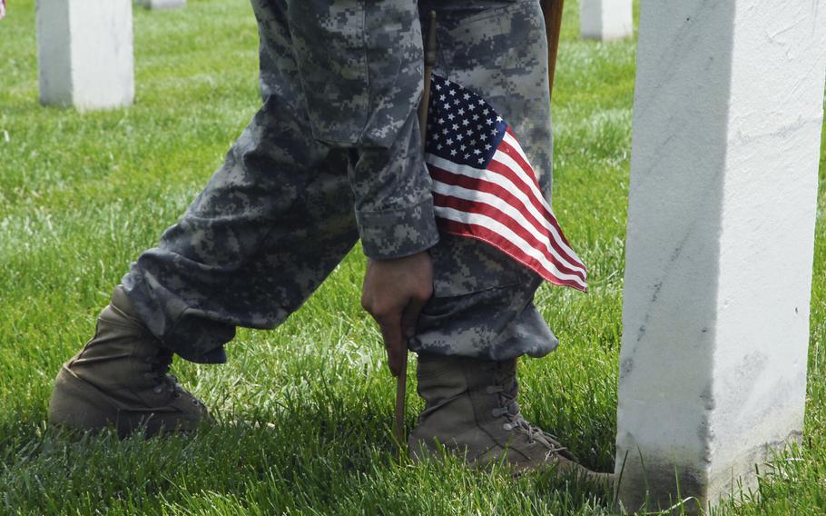 A soldier plants flags at graves at Arlington National Cemetery on May 22, 2014 as part of a "Flags In" ceremony to honor fallen troops for Memorial Day. Soldiers would place their boot against a gravestone and plant a flag at the heel to achieve a uniform look across the cemetery.