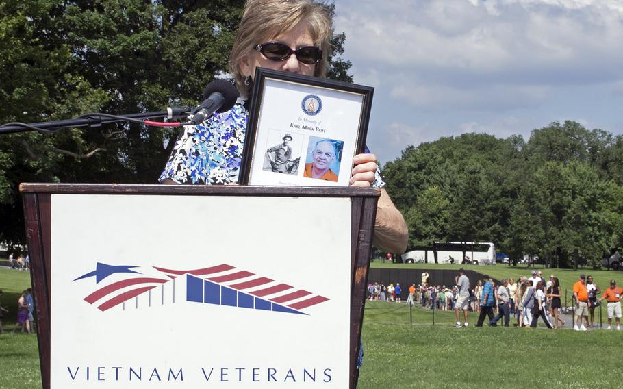 A woman reads the name of a Vietnam veteran at the In Memory Day observance on Saturday, June 14, 2014. The Vietnam Wall is seen behind her. 