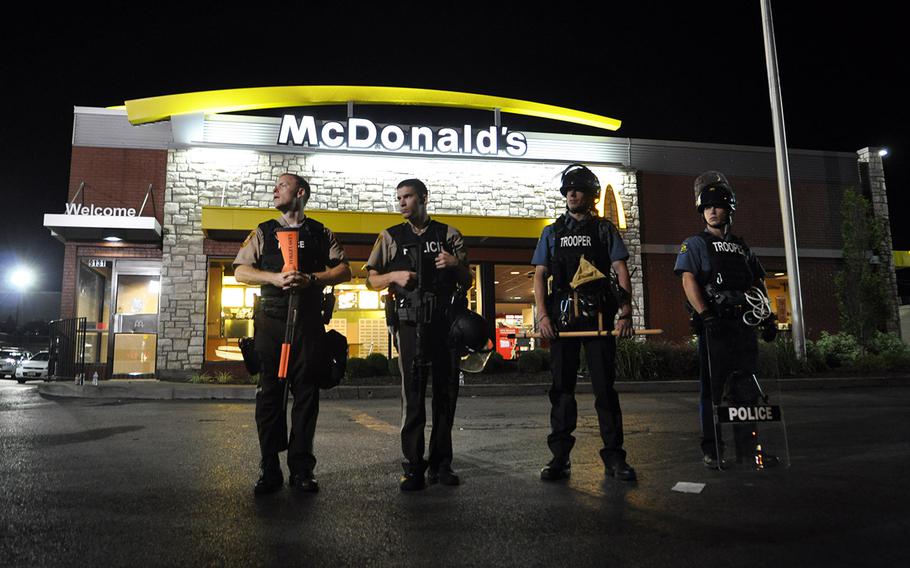 Police in riot gear stand outside a McDonald's in Ferguson, Mo., Tuesday night. Protests over the shooting of a black teen by a white police officer have escalated into riots in the St. Louis suburb and the local authorities' response has sparked a national debate about the militarization of police.