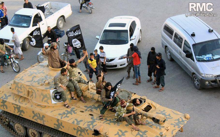 In this undated file image posted by the Raqqa Media Center of the Islamic State group Monday, June 30, 2014, which has been verified and is consistent with other AP reporting, fighters from Islamic State group sit on their tank during a parade in Raqqa, Syria.