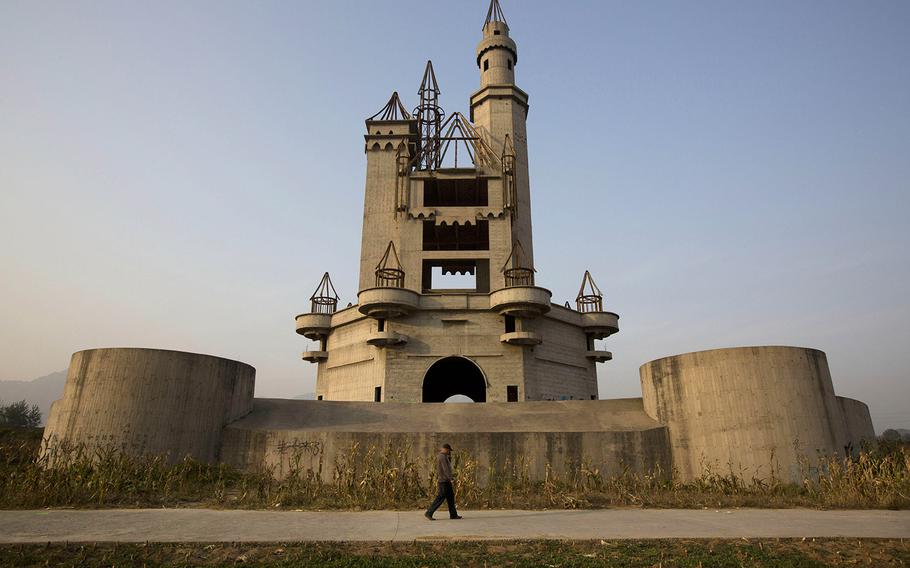 In this Oct. 18, 2014, photo, a man walks past the shell of a castle-like building that was once destined to be part of Asia's biggest amusement park in Beijing, China. Work halted on the project in 1998 due to financial problems and the site has been left as it is until 2013 when developers demolished other parts of the massive park for redevelopment. The castle-like building however remains untouched and a reminder of better times in that part of Beijing's periphery.