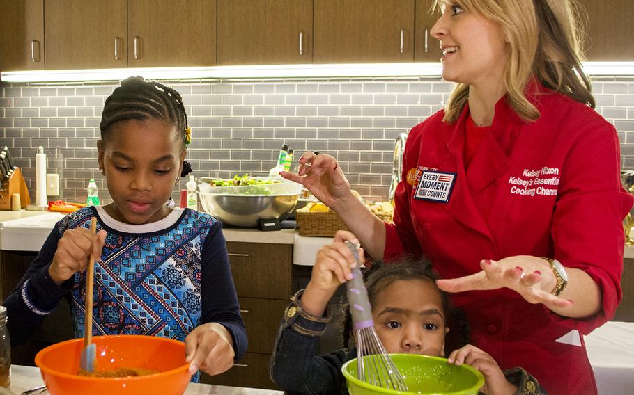Two little girls help with a cooking demonstration with Kelsey Nixon, far right, during the Make a Moment Campaign on Nov. 20, 2014, at the USO in Bethesda, Md. 