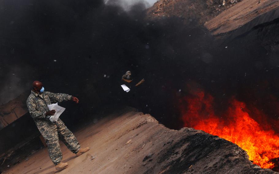 An airman tosses unserviceable uniform items into a burn pit, March 10, 2008 at Balad Air Base in Iraq.