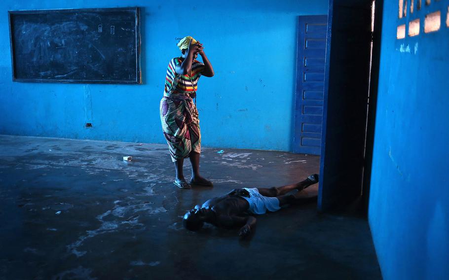John Moore, Current Affairs Photographer of the Year | Omu Fahnbulleh stands over her husband Ibrahim after he fell and died in a classroom used for Ebola patients. In the summer of 2014 Monrovia, Liberia became the epicenter of the West African Ebola epidemic, the worst in history. Although previous rural outbreaks were more easily contained, once the virus began spreading in Monrovia's dense urban environment, the results were described by Medecins Sans Frontieres as "catastrophic".