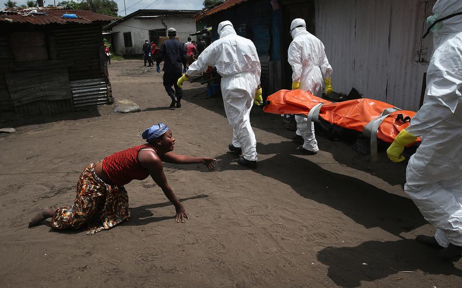 John Moore, Current Affairs Photographer of the Year | A woman crawls towards the body of her sister as Ebola burial team members take her away. With a tradition of burial rites that include the washing of the dead bodies of loved ones, Liberians became infected at alarming rates.
