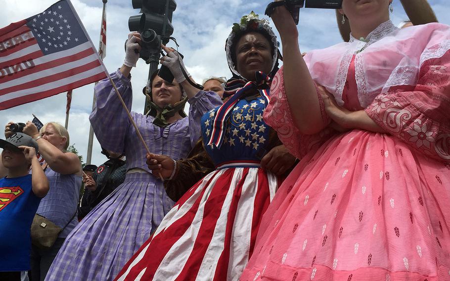 Reenactors mix costumes and modern technology as they watch from the sidewalk while troops march by in Washington, D.C., on Sunday, May 17, 2015. 