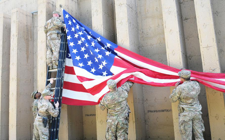 Members of the U.S. National Support Element and the Resolute Support Headquarters Forward Support Battalion hang an American flag inside the compound barrier wall in preparation for the camp's Fourth of July cookout. About 1,300 U.S. military members and civilians live and work at the camp, a NATO base in Kabul, Afghanistan. The FSB Soldiers are from the Connecticut National Guard, while the NSE Soldiers are with the 3rd Infantry Division.