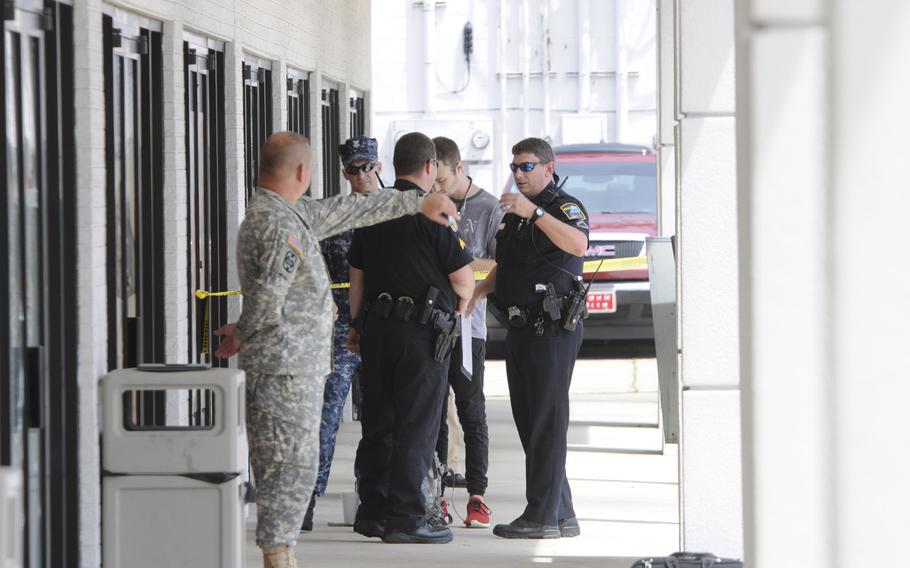 Authorities talk to workers at a Navy and Marine Corps recruitment center in Chattanooga, Tenn., where a gunman opened fire Thursday, July 16, 2015. Yellow tape cordoned off an area with blue shell casing markers in the parking lot.