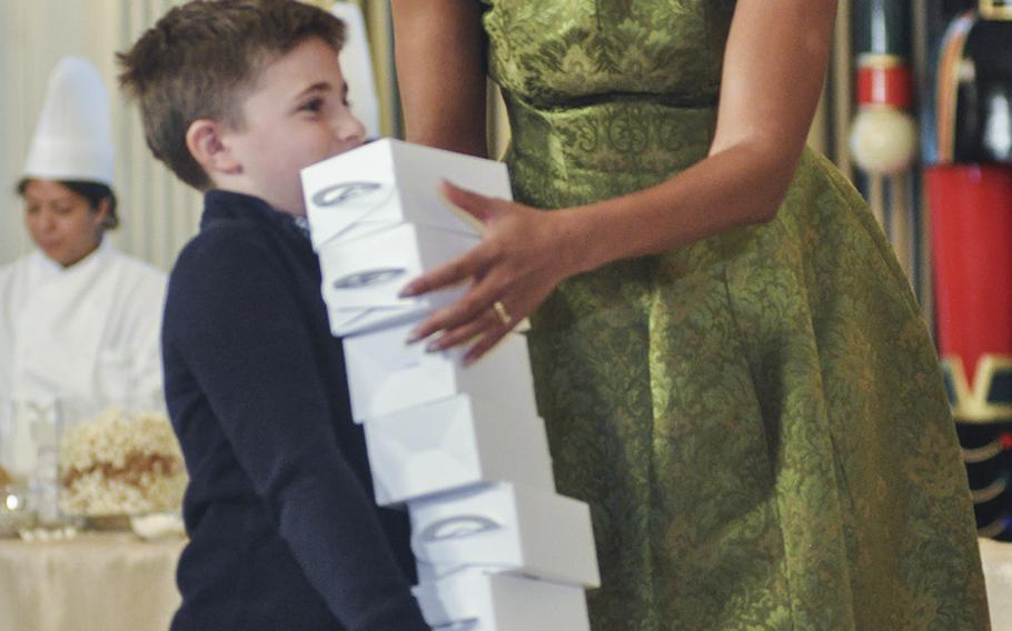 First Lady Michelle Obama lends a helping hand to a boy overloaded with cookies and popcorn at the White House on Dec. 2, 2015. Obama hosted a preview of White House decorations for military families on Dec. 2, 2015.